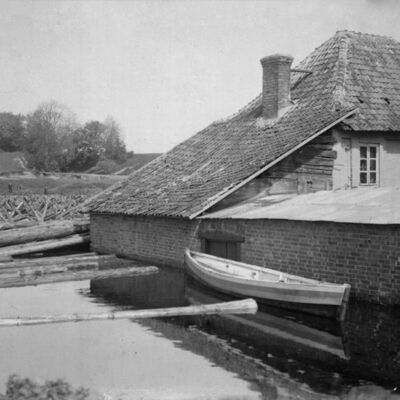 Applūdušais nams Upes ielā 1 (Kārļa Bergholca podniecība) un kokmateriālu sastrēgums Mēmelē aiz tā. Gandrīz vienā rakursā tapušās fotogrāfijas ataino divas plūdu stadijas ar aptuveni divu metru ūdens līmeņa starpību.