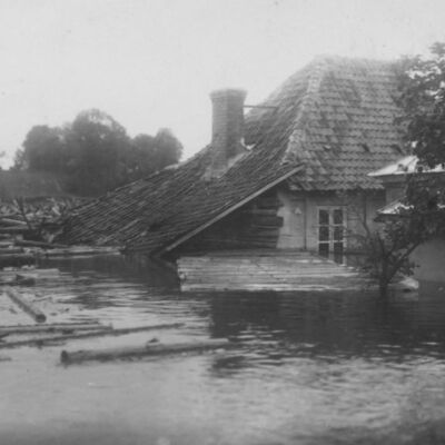 Applūdušais nams Upes ielā 1 (Kārļa Bergholca podniecība) un kokmateriālu sastrēgums Mēmelē aiz tā. Gandrīz vienā rakursā tapušās fotogrāfijas ataino divas plūdu stadijas ar aptuveni divu metru ūdens līmeņa starpību.